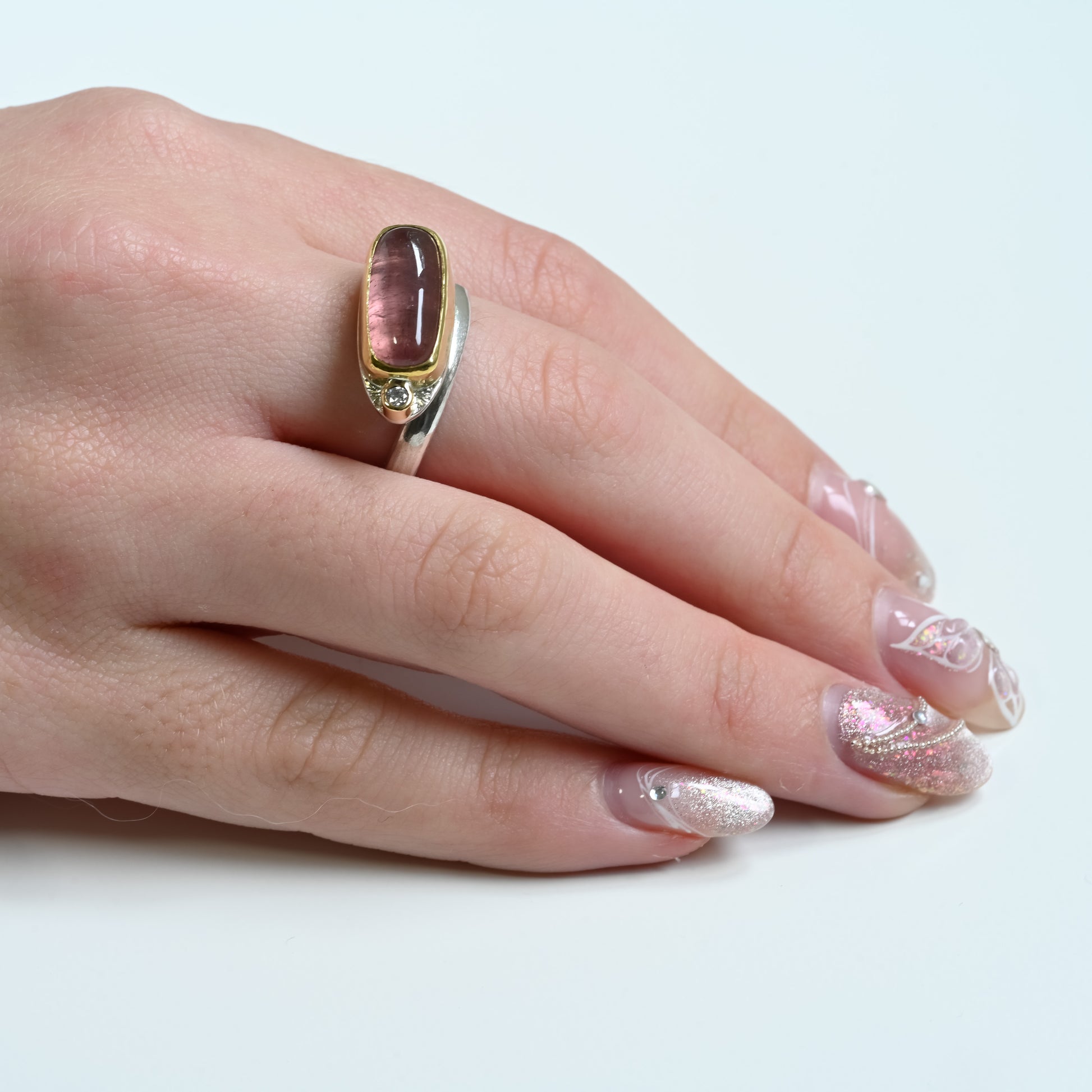 Hand wearing a gold and silver ring with a pink gemstone tourmaline on a white background
