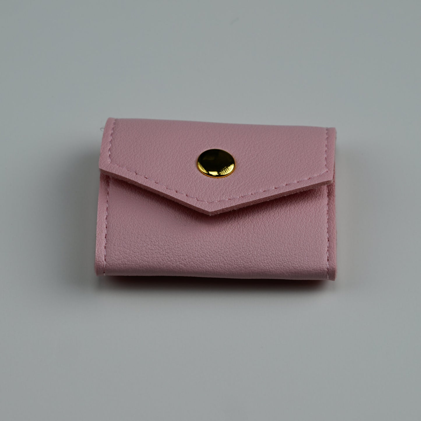 Pink faux-leather envelope jewellery pouch with gold snap, closed