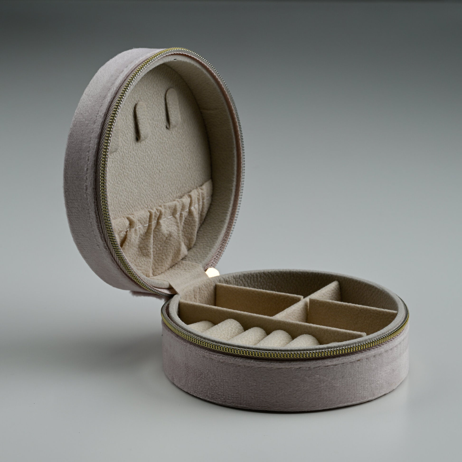 Open blush round velvet jewellery box showing ring rolls and lid pocket