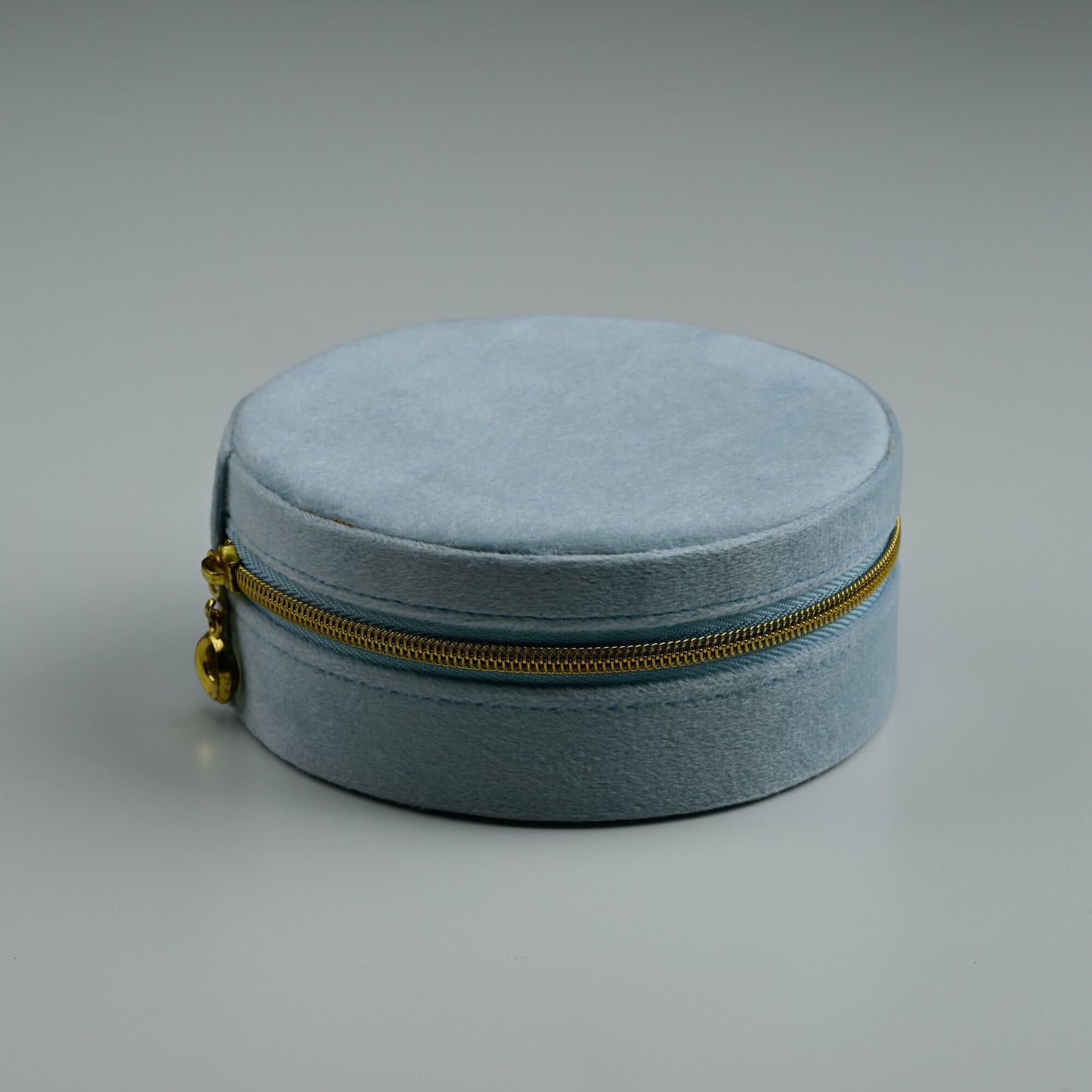 Dusty blue round velvet jewellery box with gold zip, closed