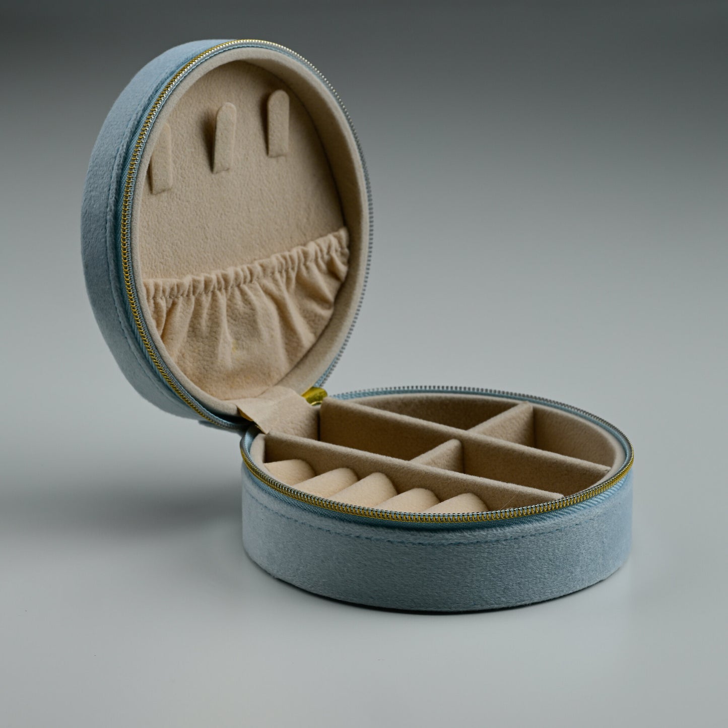 Open dusty blue round velvet jewellery box showing ring rolls and compartments
