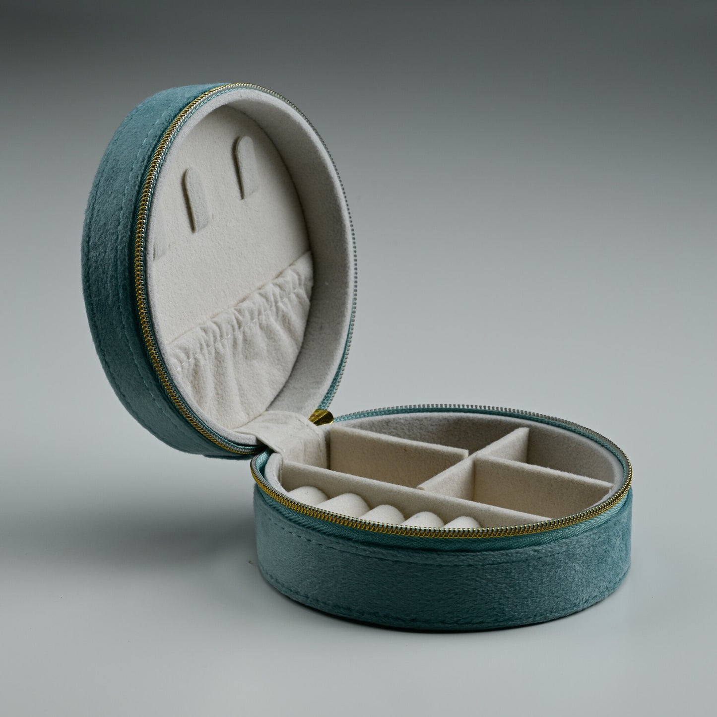 Open teal round velvet jewellery box with cream lined compartments