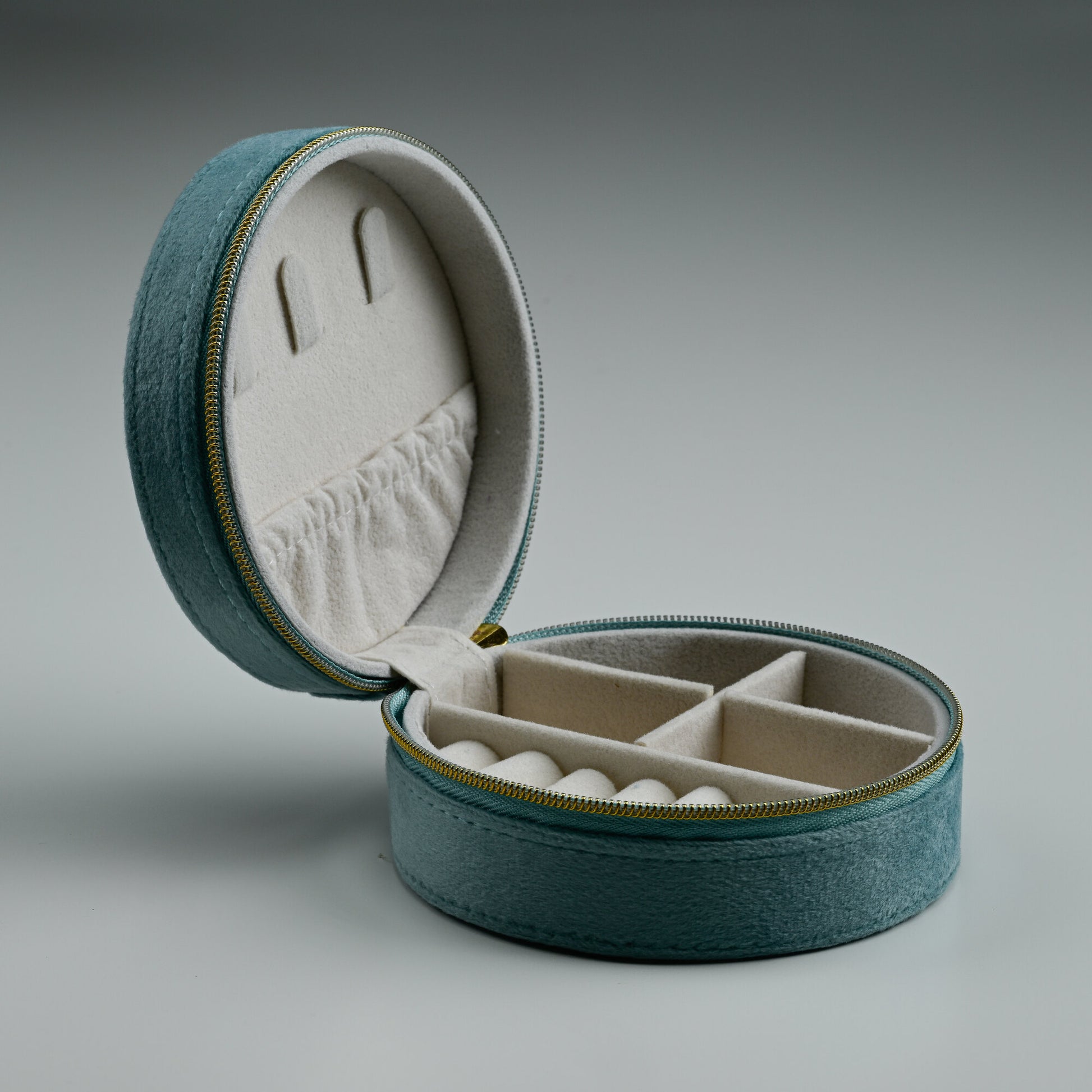 Open teal round velvet jewellery box with cream lined compartments