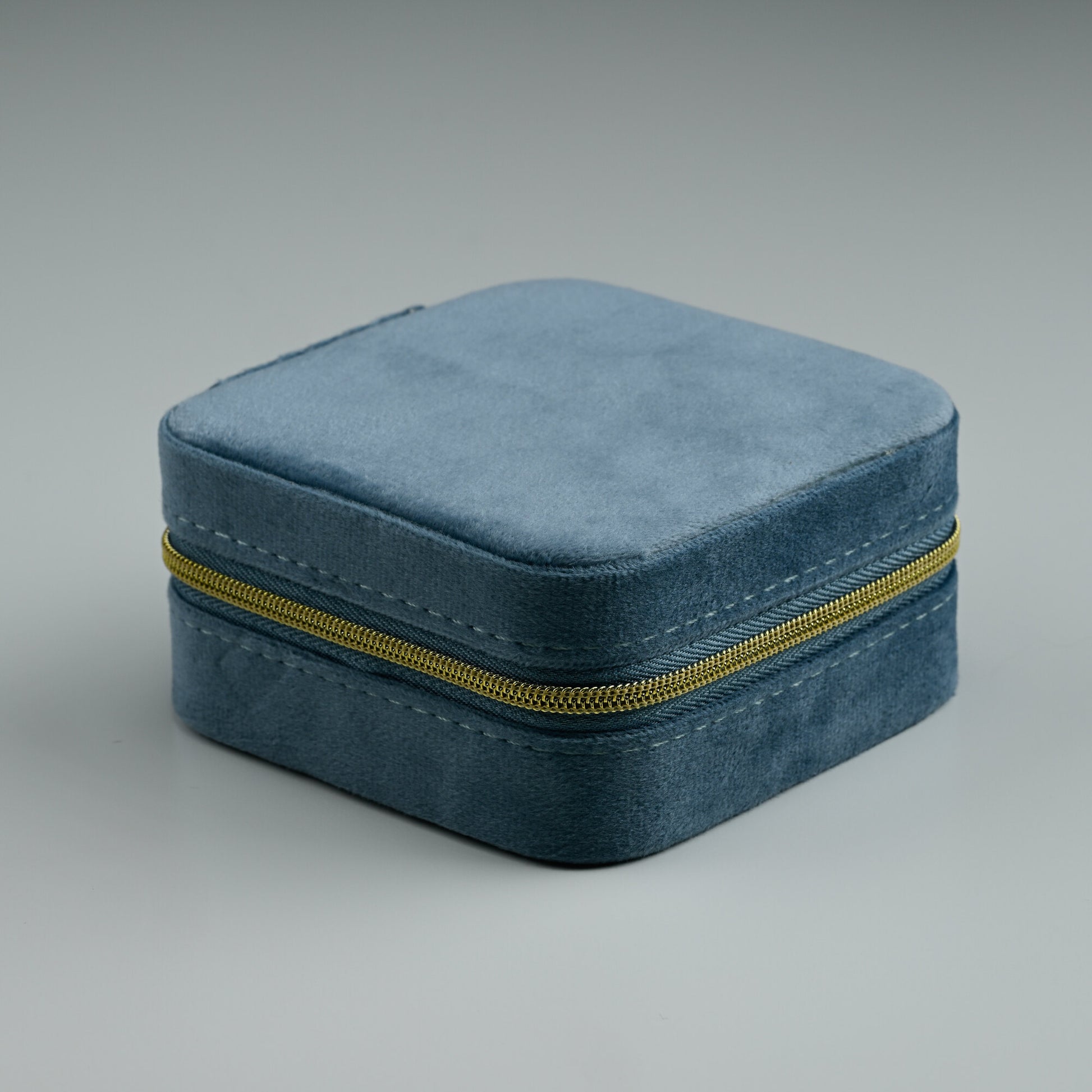 Dusty blue square velvet travel jewellery box with gold zip, closed
